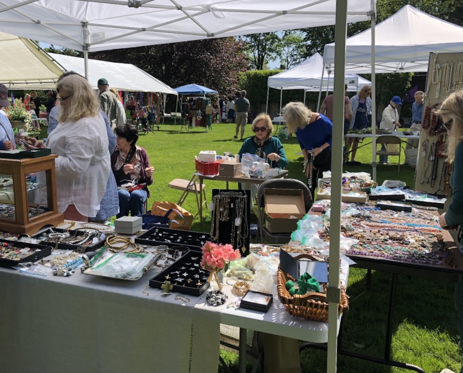 people looking over jewelry at a table under a tent at saint johns annual bazaar in southampton new york